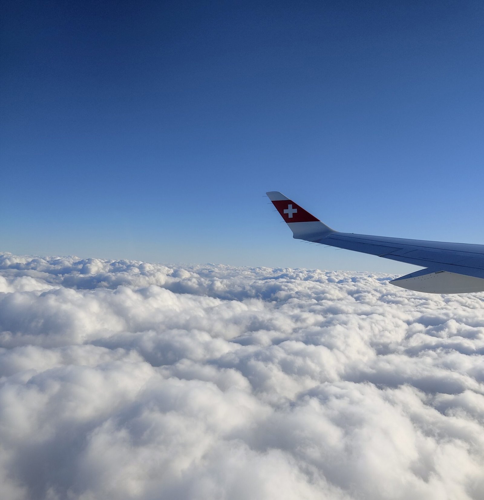 Airplane flying with the Swiss flag among clouds and blue sky, representing Cyberfulness and mindful digital well-being.