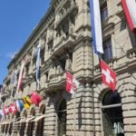 Swiss cantonal flags flying in front of a government building in Switzerland, symbolizing federal and cantonal collaboration.