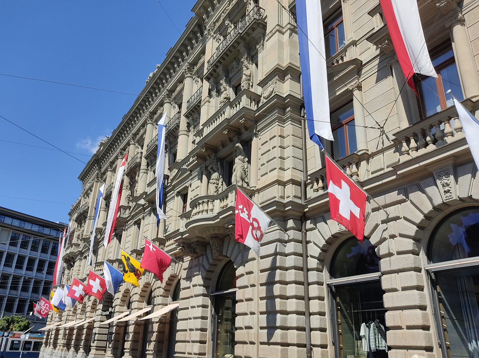 Swiss cantonal flags flying in front of a government building in Switzerland, symbolizing federal and cantonal collaboration.