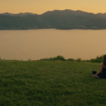 Woman meditating on a hill at sunset overlooking lake and mountains, representing cyberfulness, mindful living and longevity lifestyle
